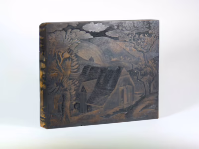 A woodblock showing a carving of a tree and house.